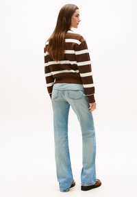 Maglione a righe marroni e bianche con una vestibilità rilassata, abbinato a jeans a flared blu chiaro. Texture morbide, cuciture visibili e hardware minimale.