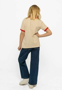 Camiseta beige con cuello y puños de manga acanalados en rojo, combinada con jeans de corte ancho. El conjunto presenta un ajuste relajado y una tela suave.