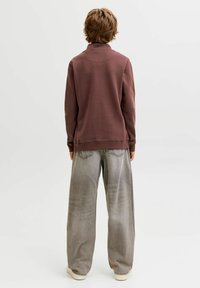 Pull marron à col montant, associé à un jean large gris clair. Le tissu semble doux, avec une coupe décontractée et un design minimaliste.