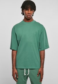 Tricou verde supradimensionat din bumbac, cu guler rotund și mâneci scurte, având o textură netedă; asortat cu pantaloni corespunzători.