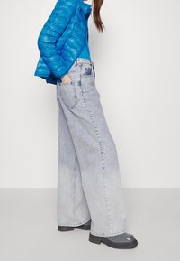 Jasnoniebieskie szerokie jeansy z wyblakłego dżinsu, zestawione z jaskrawoniebieską puchową kurtką. Stylizacja charakteryzuje się gładką fakturą i casualowym designem.