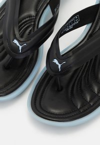 Black Puma flip-flops with cushioned soles and light blue edges, featuring the Puma logo on the straps and size label inside.