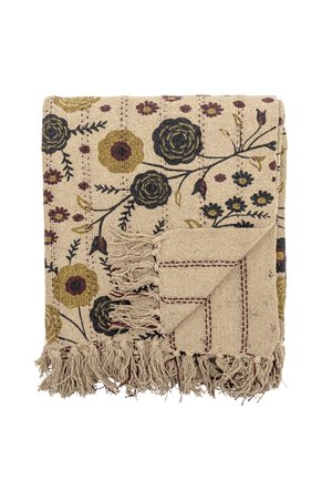Couverture tissée beige pliée avec des motifs floraux en noir, moutarde et bordeaux, avec des franges le long des bords et un détail cousu dans le coin.
