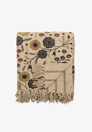 Couverture tissée beige pliée avec des motifs floraux en noir, moutarde et bordeaux, avec des franges le long des bords et un détail cousu dans le coin.