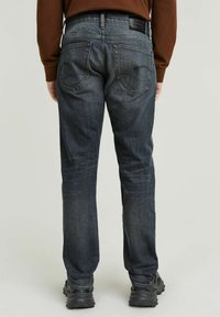 Donkerblauwe denim jeans met een recht gesneden ontwerp, voorzien van achterzakken en een merkgeborduurde tailleband. Zachte textuur, minimale vervaging.