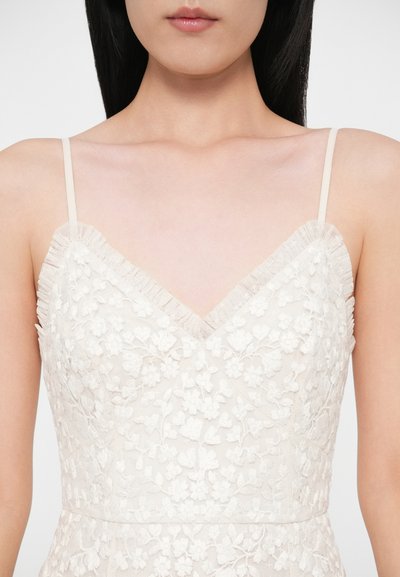 Το δαντελωτό φόρεμα διαθέτει V-λαιμόκοψη, λεπτή κεντητική με λουλουδένιο μοτίβο, ρυθμιζόμενους λεπτούς ιμάντες και απαλό, κρεμ χρώμα με διακριτικές πινελιές από βολάν.