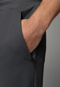 Grijze textuurshorts met een ritszak en een elastische tailleband, met een close-up van de hand in de zak.