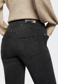 Jeans elásticos negros con una cintura alta, que cuentan con dos bolsillos traseros y una etiqueta de cuero negro con marca en la parte trasera de la cintura.