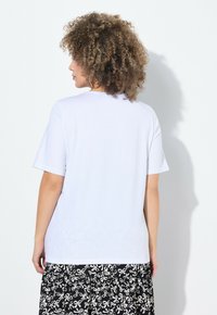 Camiseta de algodón blanca con mangas cortas, un cuello redondo y un corte relajado, combinada con una falda negra con un diseño estampado.
