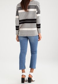 Czarnobiały sweter w paski z dzianiny, zestawiony z niebieskimi, skróconymi jeansami oraz białymi sandałami na klocku, prezentujący teksturowany wzór.