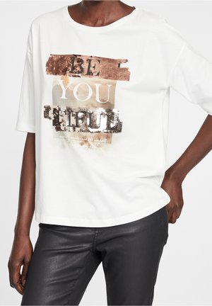 Camiseta de manga corta blanca con lentejuelas metálicas color oro rosa y el texto "SÉ TÚ" en negrita. Ajuste holgado y material de algodón suave.