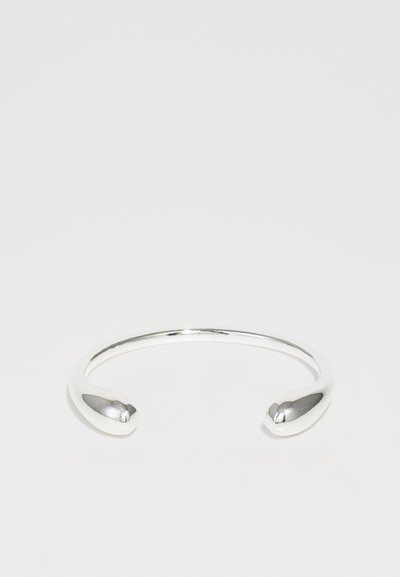 Bracelet en argent avec un design lisse et minimaliste et des extrémités effilées. La surface a une finition polie et une forme uniforme.