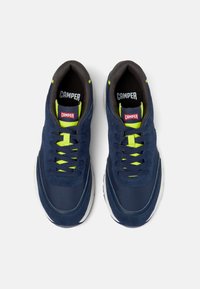 Sneakers blu scuro con accenti gialli riflettenti, caratterizzati da un design con lacci e il logo 'Camper' sulla linguetta.