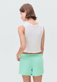 Bílý, texturovaný crop top s nerozřezanými okraji v kombinaci s mátově zelenými, středně vysokými šortkami s volným střihem a třepeným lemem.