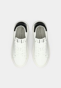 Λευκά δερμάτινα αθλητικά παπούτσια με μαύρο επενδυμένο γιακά, επίπεδα κορδόνια και λογότυπο στη γλώσσα. Διαθέτουν ομαλή υφή και μινιμαλιστικό σχεδιασμό.