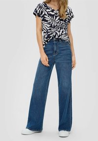 Haut à manches courtes bleu marine à motifs floraux blancs, associé à un jean large en denim bleu. Coupe décontractée et texture en denim léger. Baskets blanches.