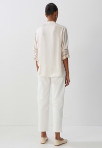 Blusa a maniche lunghe beige chiaro con polsini arrotolati abbinata a pantaloni bianchi a gamba dritta e scarpe flat beige. Tessuto morbido, design minimale.