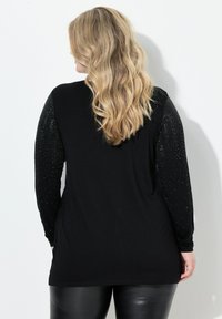 Svart långärmad topp med dekorerade texturerade ärmar, med en slät kropp och avslappnad passform, parat med svarta byxor i imiteträ.