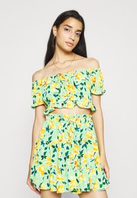 Completo floreale a due pezzi composto da un top verde a spalle scoperte con fiori gialli e arancioni e una gonna a strati abbinata con vita elasticizzata.