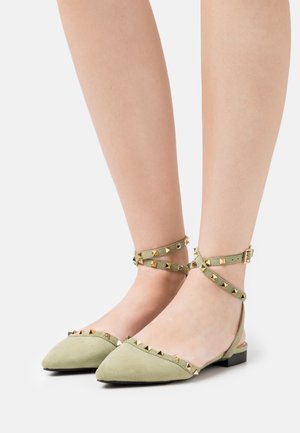 Pointed-toe flat shoes in light green suede with gold-tone pyramid studs and ankle straps, featuring a low block heel.