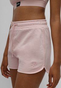 Růžové tepláky s elastickým pasem, stahovací šňůrkou a vyšitým logem. Měkká tkanina s hladkým povrchem a zakřiveným lemem.