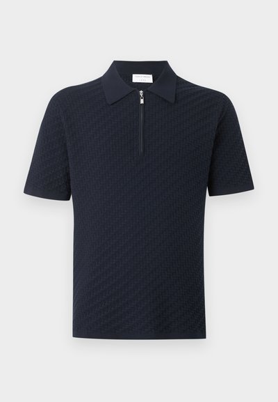 Πόλο μπλούζα σε σκούρο μπλε χρώμα με κοντά μανίκια, υφασμένο σχέδιο και φερμουάρ μπροστά που εκτείνεται από τον γιακά μέχρι το στήθος.