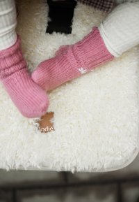 Baby wearing pink knitted booties lying on a soft, white textured blanket with a brown leather tag.