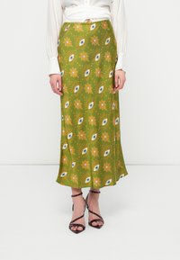 Saia maxi verde claro com um padrão repetido de olhos e flores em amarelo e azul, com uma textura suave e um design fluido.