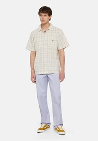 Lys rutete kortermet skjorte med knapper, i beige og lyseblå farger, sammen med lilla rette bukser og gule sneakers.