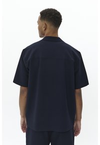 Camicia a maniche corte blu navy in tessuto testurizzato, con colletto alla francese e orlo dritto, mostrata da dietro.