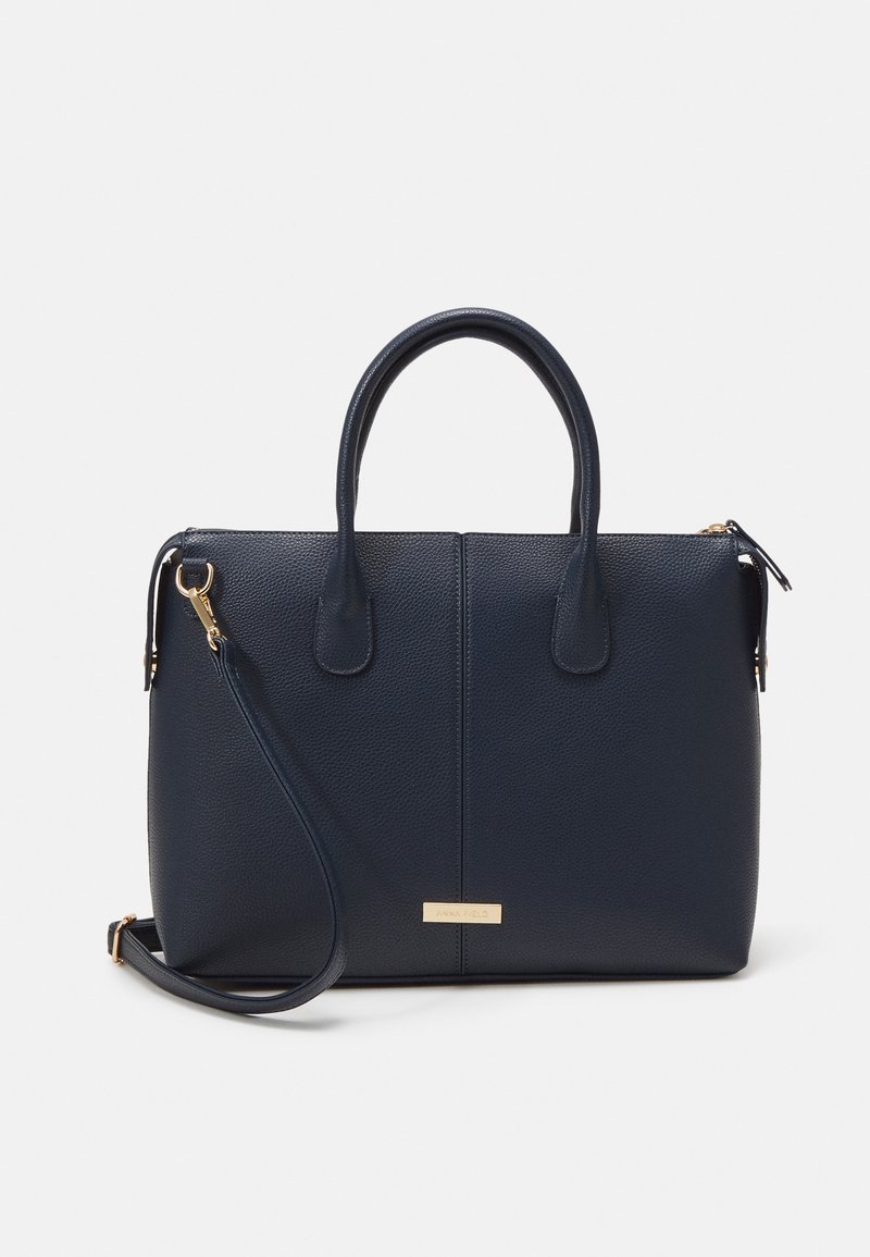 Sac à main en cuir bleu marine avec deux poignées, une bandoulière amovible et des ferrures dorées sur un fond clair uni.