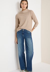 Suéter beige acanalado con cuello vuelto, combinado con vaqueros de pierna ancha en azul. Los vaqueros tienen cierre de botón y un sutil efecto desgastado.