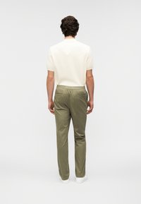 Polo à manches courtes crème, pantalon vert olive avec taille élastique, poches latérales, et baskets blanches, vu de dos.