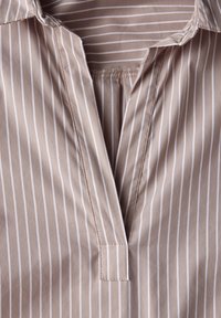 Camicia di cotone beige con strisce bianche verticali. Presenta un scollo a V, colletto piegato e una leggera arricciatura al collo.