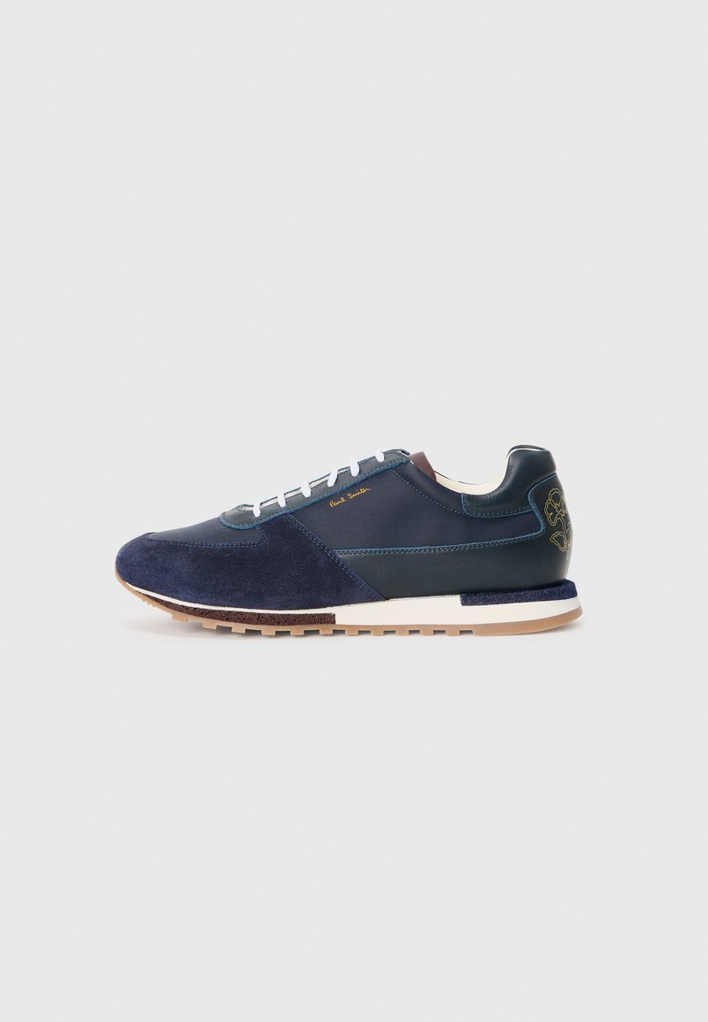 Navy blue suede and leather sneaker with white laces, a textured sole, and a brown accent at the rear featuring a logo detail.