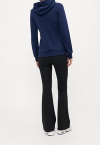 Navy blue sweatshirt with a hood and a relaxed fit, paired with black flared trousers and white sneakers. Soft, smooth fabric texture.