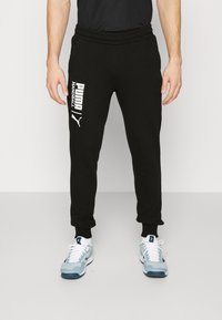 Svarte sweatpants lavet af blødt stof med elastisk talje. Har hvidt trykt tekst på venstre ben og ribbede manchetter ved anklerne.