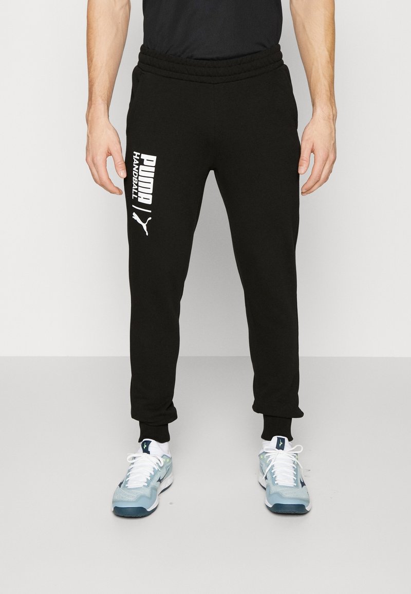 Svarte sweatpants lavet af blødt stof med elastisk talje. Har hvidt trykt tekst på venstre ben og ribbede manchetter ved anklerne.
