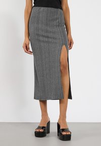 Šedá vroubkovaná midi sukně s bočním rozparkem, vyrobená z měkké elastické tkaniny. Stylizováno s robustními černými platformovými sandály.