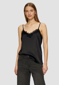 Camisole en satin noir avec des bretelles fines réglables et de la dentelle le long de l'encolure, associée à un jean foncé taille haute.