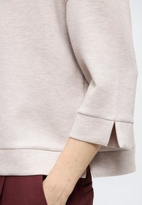 Ανοιχτό μπεζ φούτερ, άνετη εφαρμογή, με μανίκια 3/4 και σχισμές στα μανίκια. Μαλακή υφή και ίσια γραμμή στο τελείωμα που προσθέτουν στην απλότητά του.