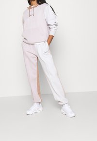 Light pink and white hoodie with a front pocket and drawstring. Complementing light pink and white sweatpants. White sneakers with textured accents.