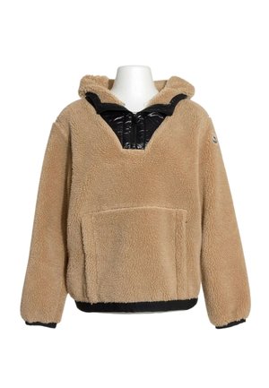 Pull à capuche en polaire beige avec un détail de fermeture éclair matelassée noir au niveau du col et une poche kangourou à l'avant sur un mannequin blanc.