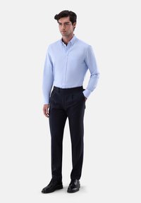 Hellblaues Button-Down-Hemd mit einer einzelnen Brusttasche, kombiniert mit dunkel gefärbten, maßgeschneiderten Hosen und schwarzen Schnürschuhen. Glattes Material, taillierte Passform.