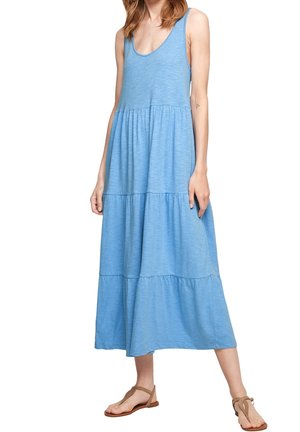 Jasnoniebieska sukienka na ramiączkach z falbanami, wykonana z miękkiego materiału. Ma dekolt w kształcie litery U i sięga do połowy łydki, zestawiona z płaskimi sandałami.