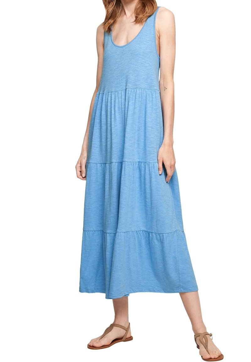 Robe débardeur bleu clair à volants, confectionnée dans un tissu doux. Elle présente un col rond et s'arrête au milieu du mollet, portée avec des sandales plates.