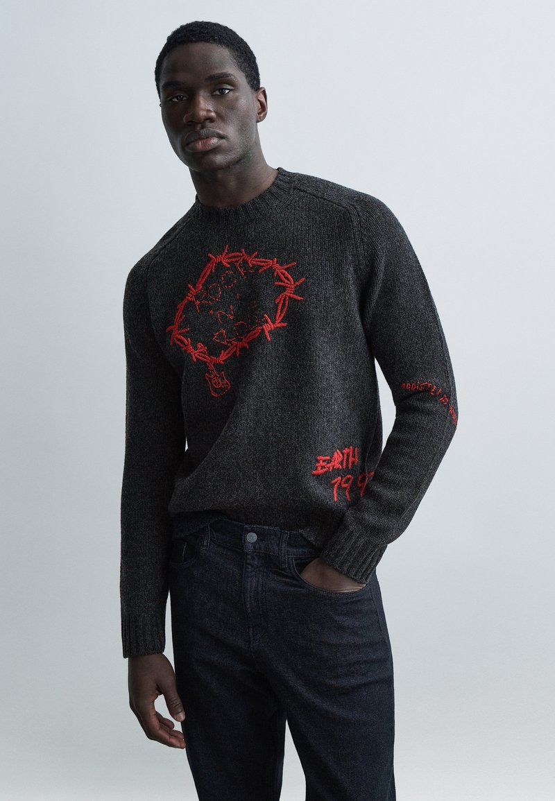 Kultrøget sweater med rød broderi, der forestiller et hjerte og tekst. Ribbet struktur, rund hals og tætsiddende ærmer. Båret med mørke jeans.