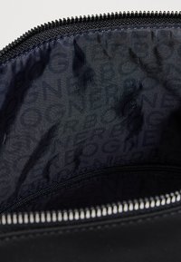 Gros plan sur la fermeture éclair ouverte d'un sac noir révélant un intérieur en tissu sombre avec un motif textuel imprimé subtil.