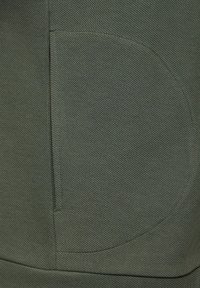 Dark green fabric with a textured surface, featuring a rounded pocket design and visible stitching detail along the edges.