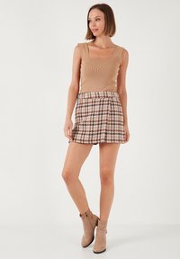 Bežasti rebrasti top s kvadratnim izrezom, uparen s mini suknjom u smeškom i kremastim uzorkom. Styling dopunjen bežčastim gležnjačama.